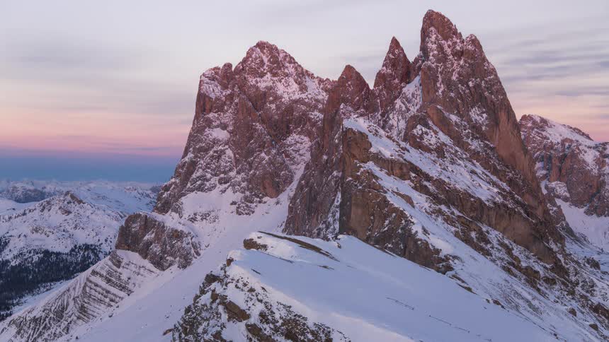 Rugged snowy mountains under a clear blue sky that begins to darken