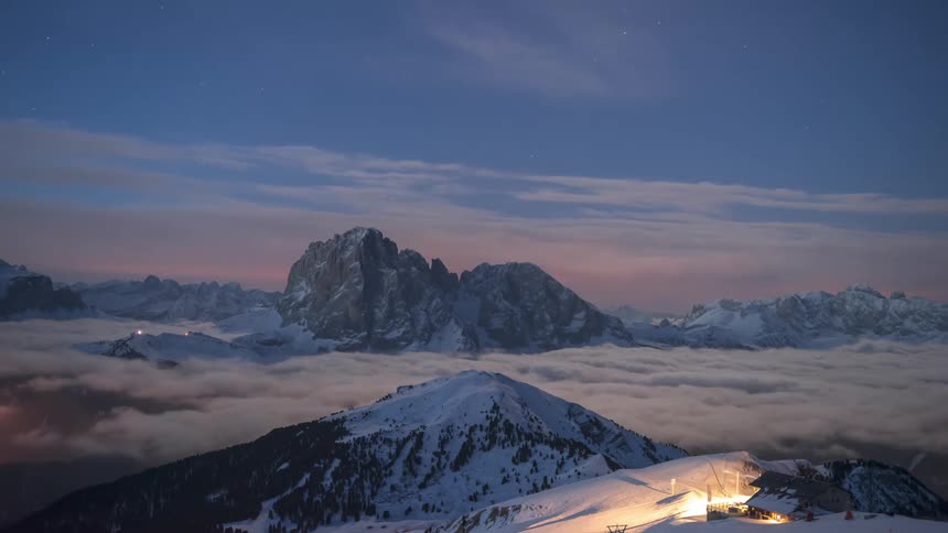 Sea of clouds near mountain peaks with snow and a small cabin isolated in the background