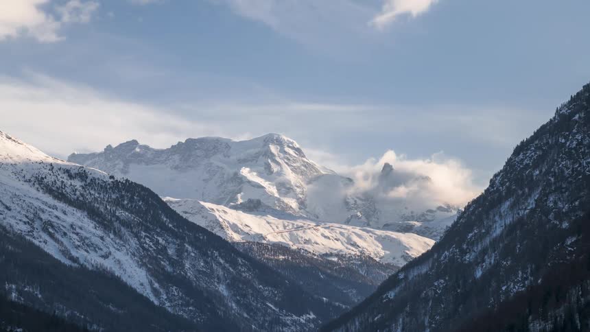 Sunlit snowcovered mountain landscape with scattered clouds