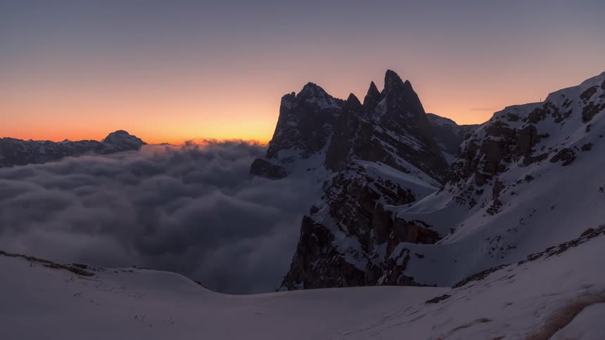 Dense clouds flow around snowy mountains in the morning
