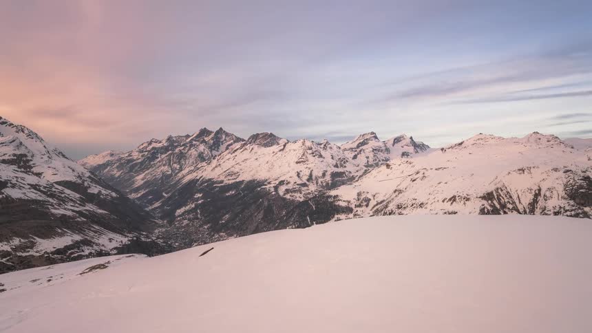 A range of mountains that are covered in white snow and clouds passing quickly in the sky