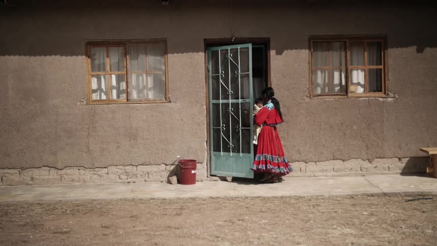 A woman carrying a baby opens a door and enters the building