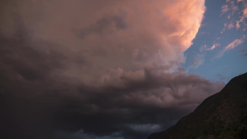 Several dark colored clouds passing through the sky and behind there is an orange cloud illuminated by sunlight