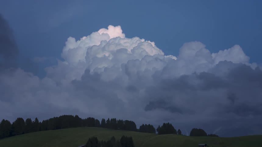 Landscape of mountains and hills with silhouettes of trees and nebulous clouds passing by