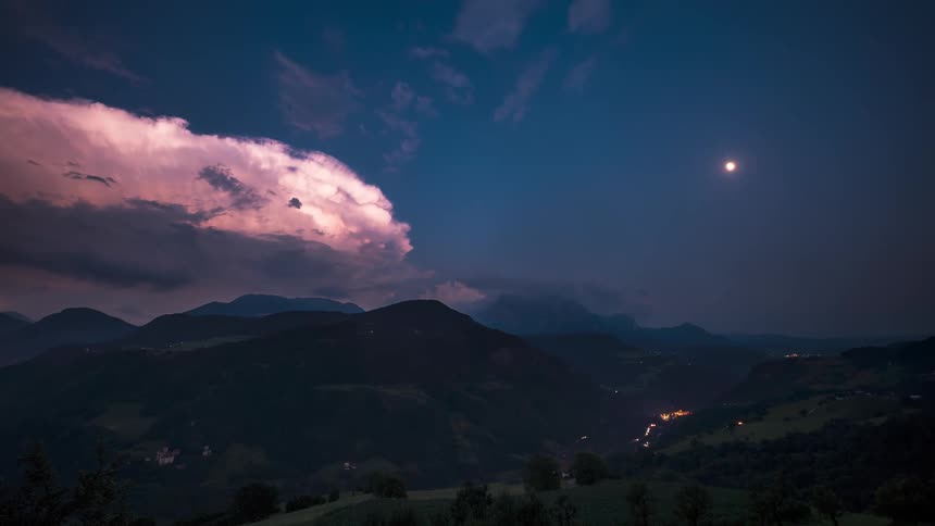 Time lapse of storm clouds rolling over a highway in the mountains at night