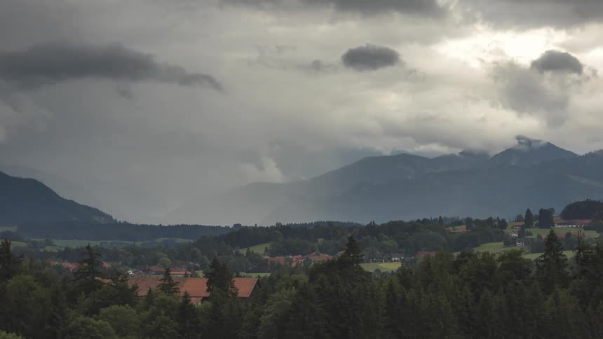 Serenity of gentle hills with vegetation and sparse buildings under a sky about to rain