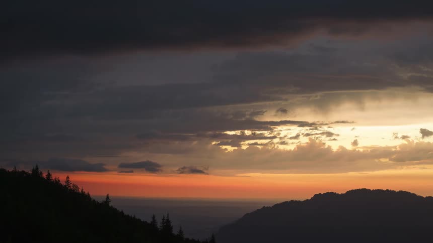 Time lapse of a sunset obscured by clouds over the mountains