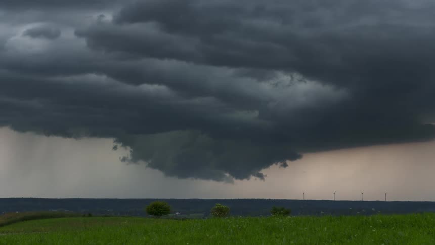 A huge gray storm cloud is moving in the sky and there is a lawn below facing the sea