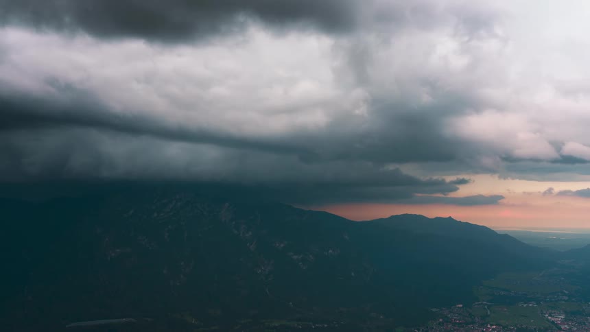 Clouds flow through the red tinted sky passing over mountains and the nearby rural town