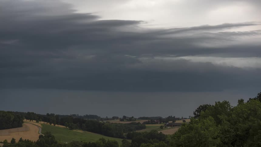 Time lapse of dark clouds rolling over a rural landscape of fields and small farms