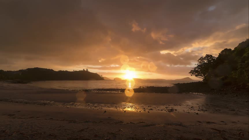 Sun flares on the horizon as the clouds flow toward the beach at sunset