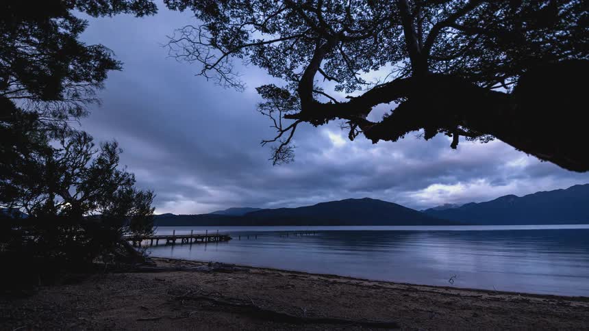 Time lapse of clouds rolling over a calm lake nested in the mountains