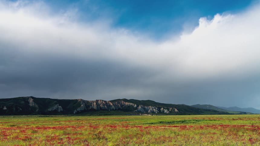 Landscape of a field with mountains in the background and clouds passing by