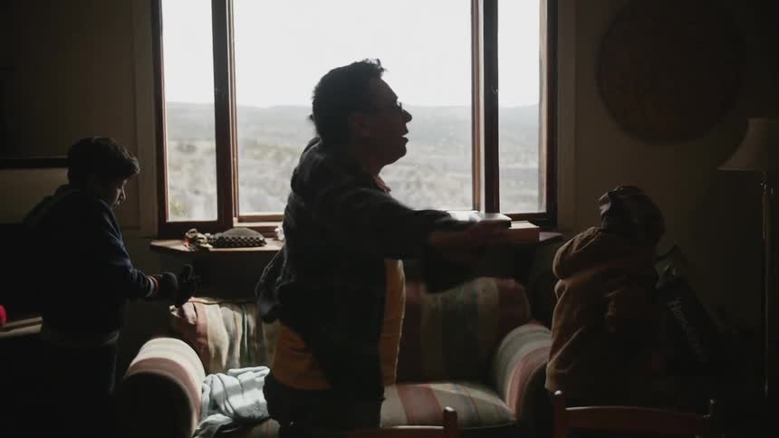 A man standing in a room with two children is putting on a jacket