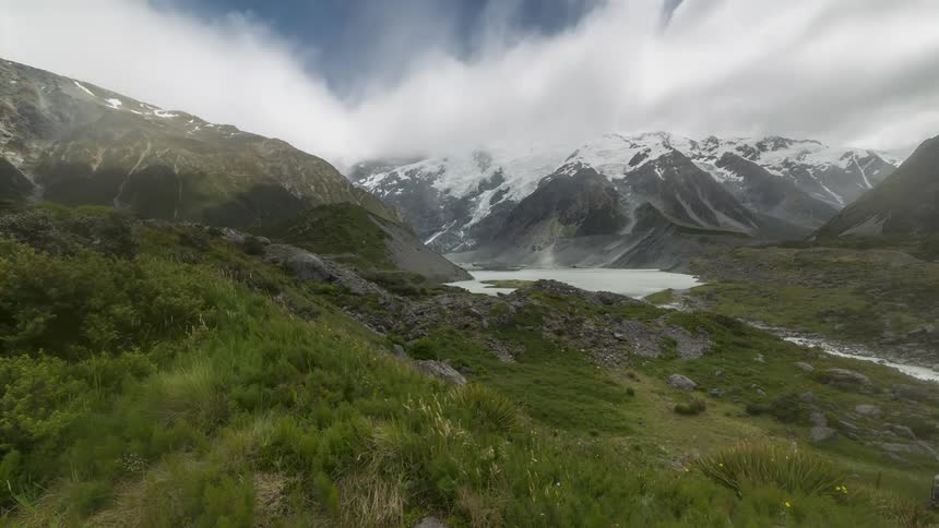 Clouds flow over a stream in a valley surrounded by snow dusted mountains on a winter day