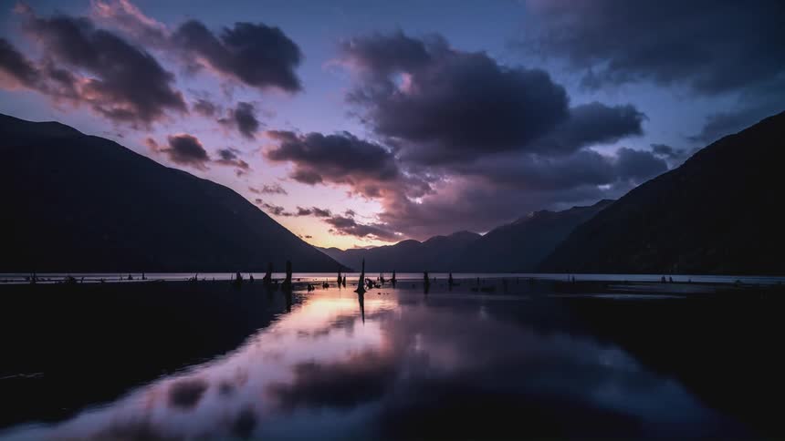 Landscape of a lake surrounded by mountains and clouds passing by as the day dawns