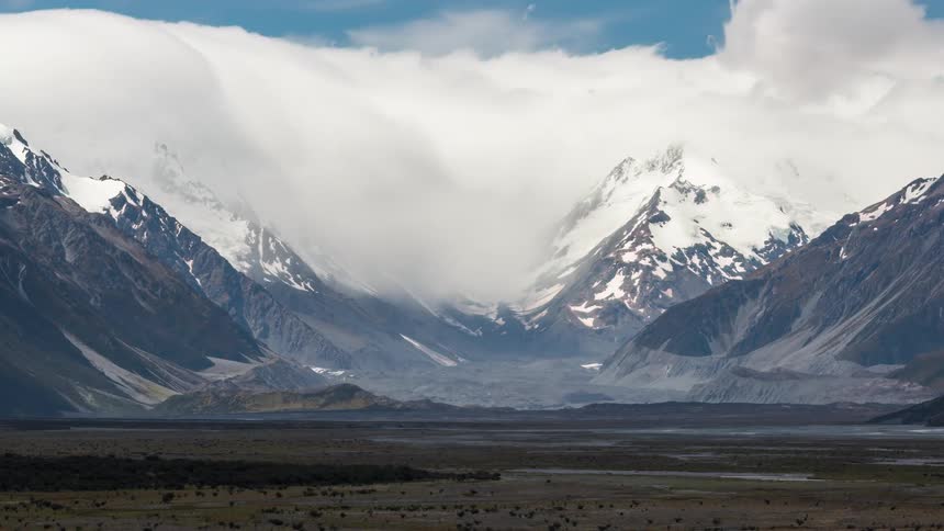 A mountain range with a snowcovered peak and white clouds passing over them