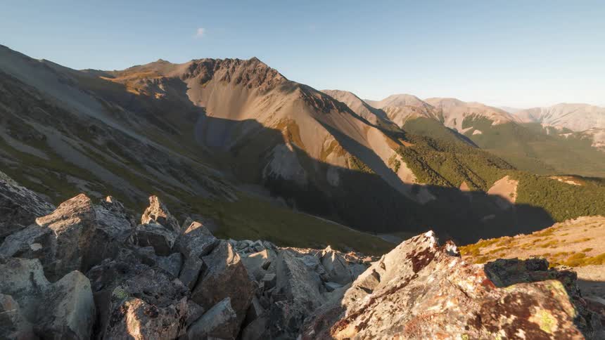 Rock strewn slope overlooks valley across from partially forested mountain range