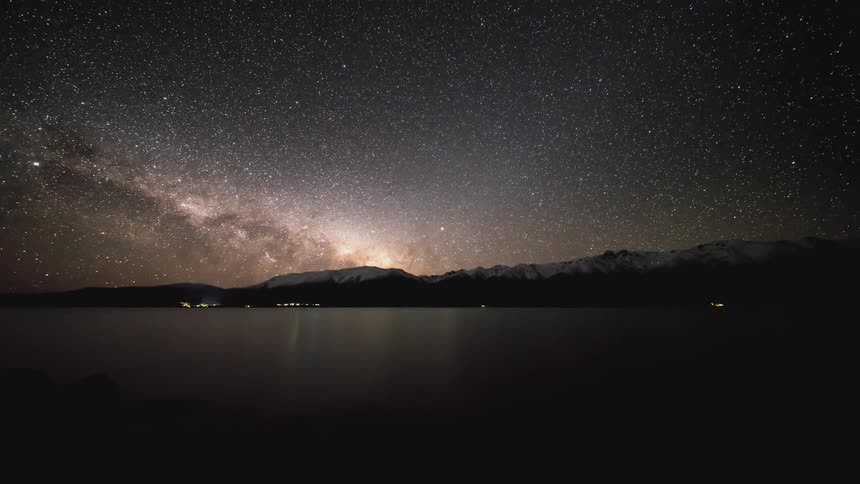 Landscape of a lake with mountains around it and a starry sky at night as the day dawns