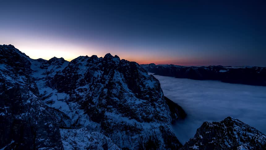 Snowcapped mountain peaks with a sea of clouds at dusk
