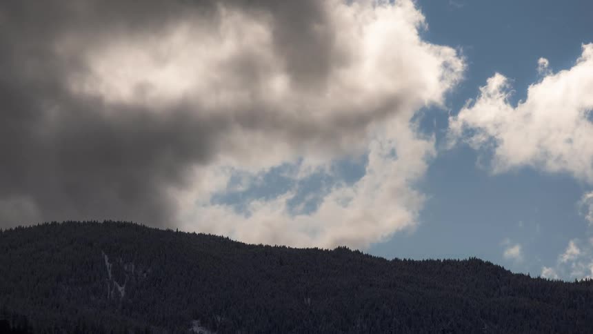 Darkening clouds roll in over a mountain covered in a forest