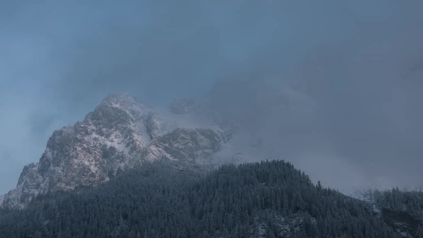 Majestic snowcapped mountain above a coniferous forest under a blue sky with mist