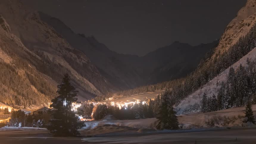 Time lapse of night falling over a small town nestled on a forest between mountains