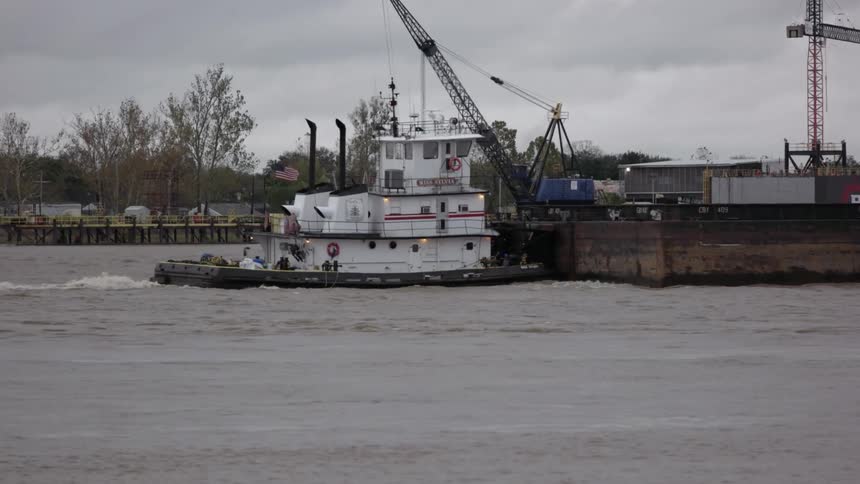 Small tugboat pushing a platform along a river on a cloudy day
