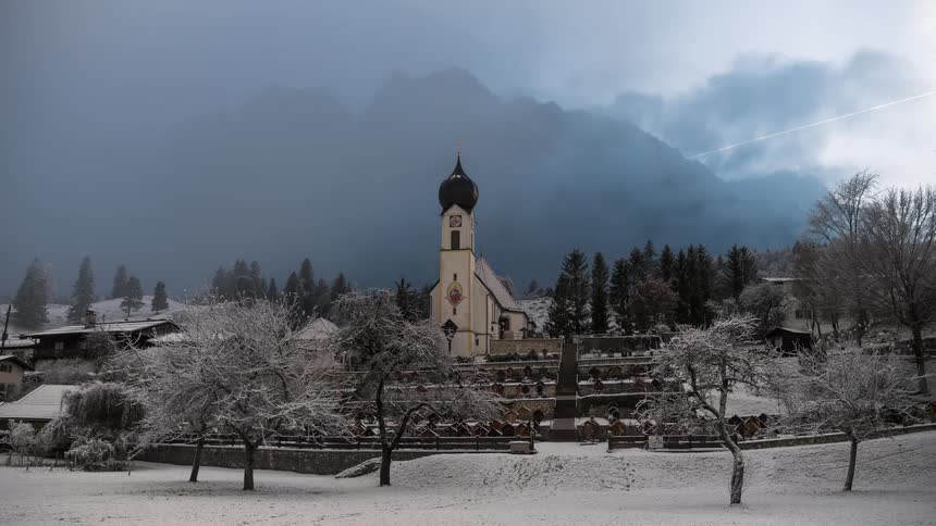 Domed building towers over snow covered houses while fog obscures the mountains in the background on a snowy winter day
