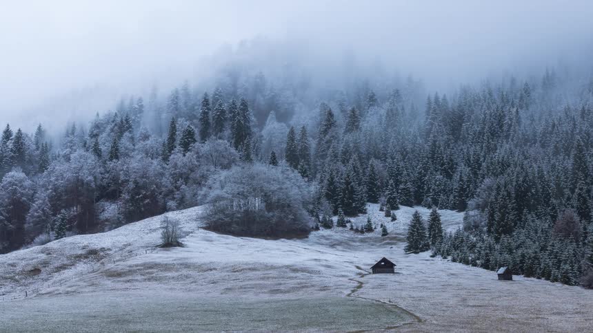 Time lapse of low clouds rolling over a winter landscape with a small cabin in the mountains