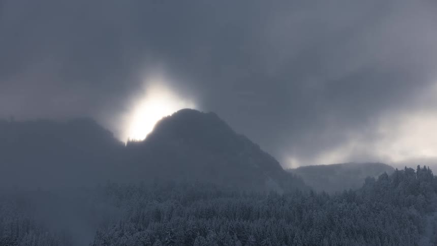 Time lapse of clouds rolling over a pine tree forest next to a snow covered mountain