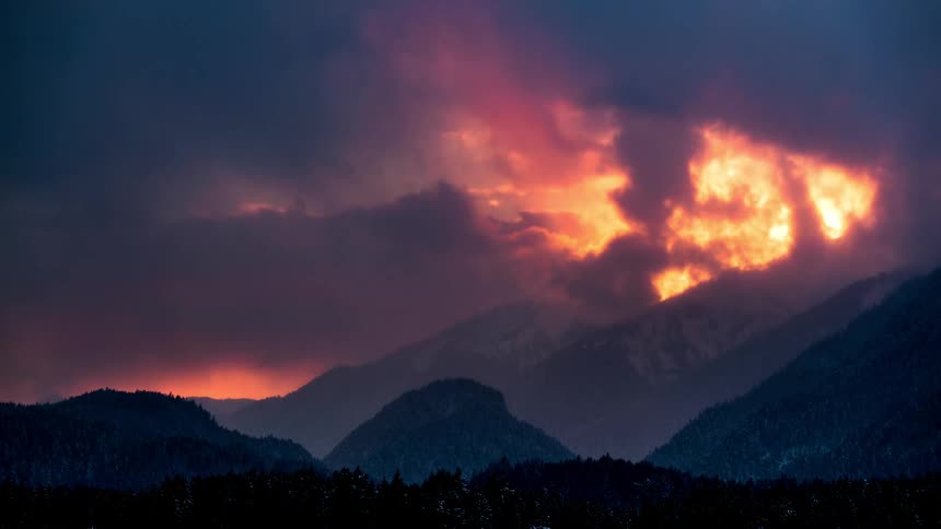 Silhouette of mountains with conifers and a reddish cloudy sky