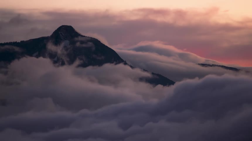 Sea of clouds passing over the silhouette of mountains as the day darkens
