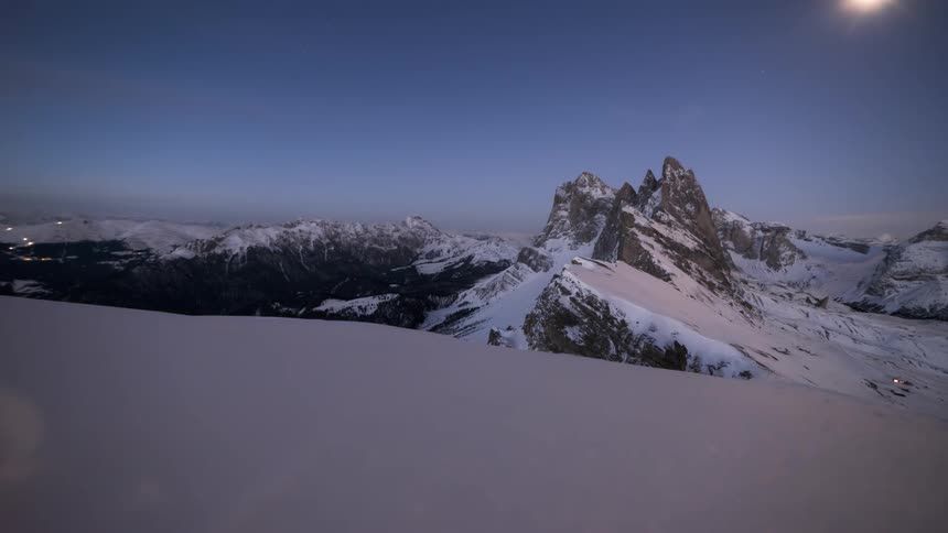 Time lapse of a bright night and the moon over a snow capped mountain range