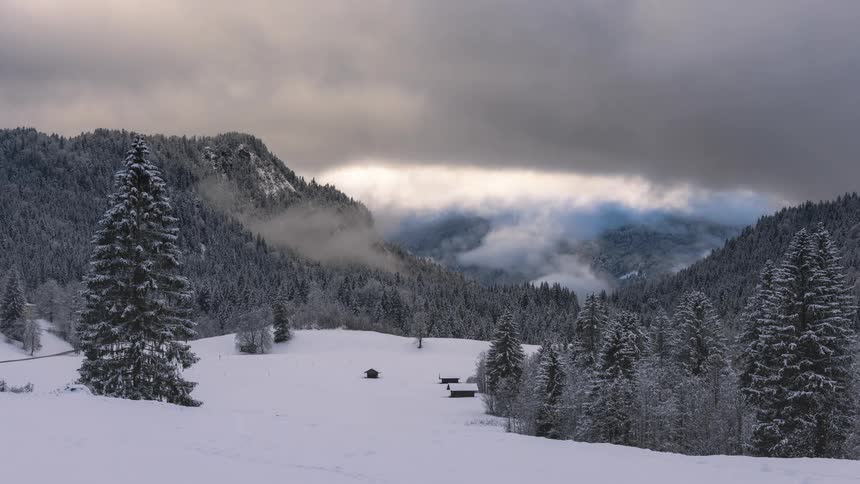 Time lapse of clouds rolling over a valley with small cabins in the woods