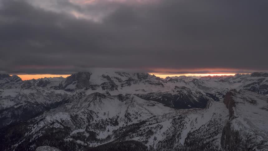 Time lapse of a thick layer of clouds rolling over the snow covered slopes of a mountain range