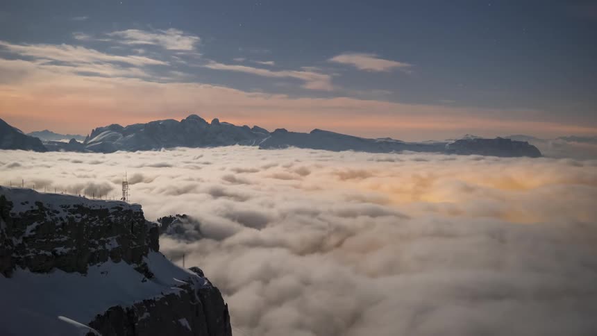 The peak of mountains covered in snow and the bottom to a horizon full of white clouds moving to the sides