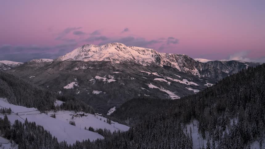 A snow covered mountain range is below a sky with clouds moving via time lapse