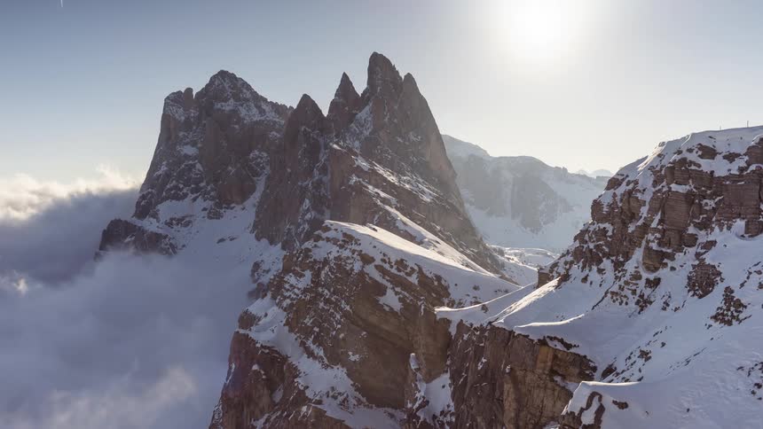 Clouds move around the side of a snowy mountain range