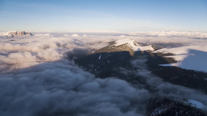 A view from the peak of a mountain range where there are several white clouds passing through the environment