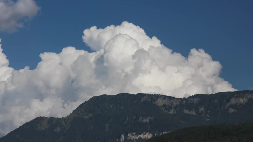 Landscape with dark mountains at the bottom and a clear blue sky dominated by large voluminous white clouds