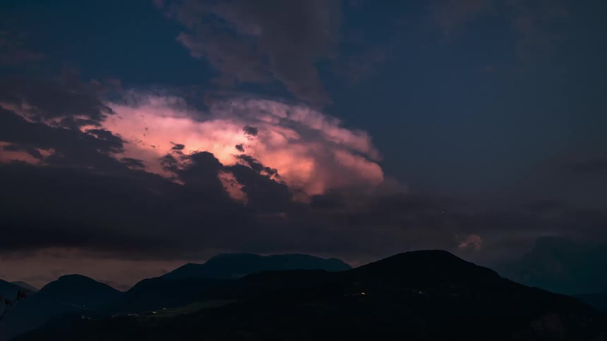 Silhouette of mountains against a reddish sky with clouds passing by