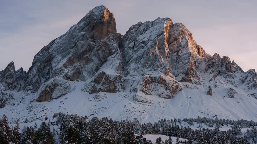 Craggy mountains tower over conifer woods during a snowy winter day