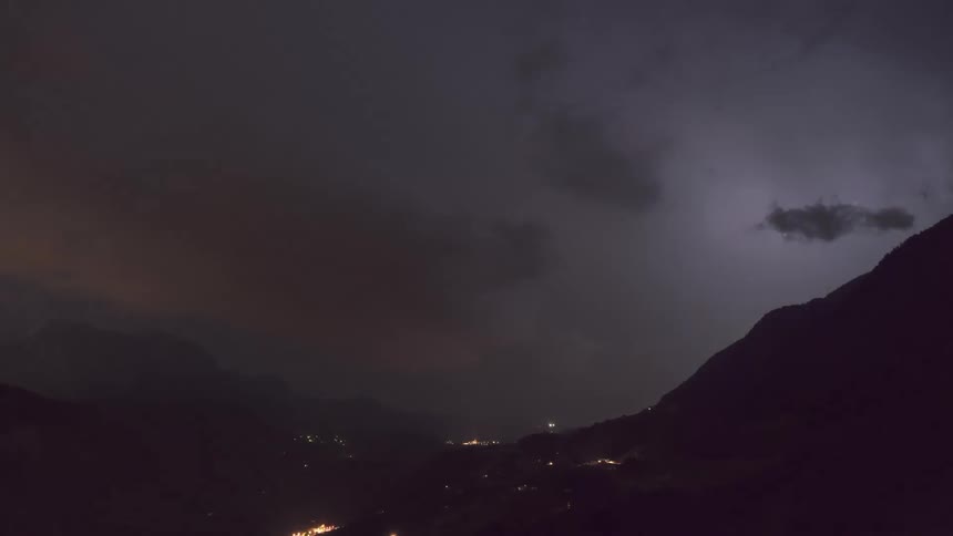 Big storms light up the sky over a rural area and roads driven on by cars