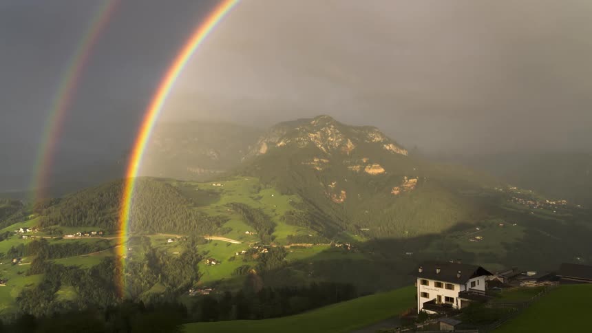 Double rainbow with a dark stormy sky over a green valley in the mountains