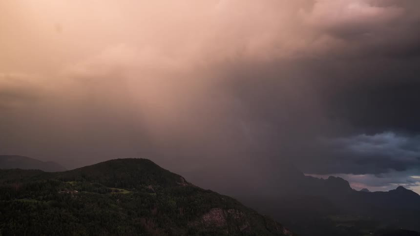 Dark storm clouds gather over a rural area and the surrounding mountains