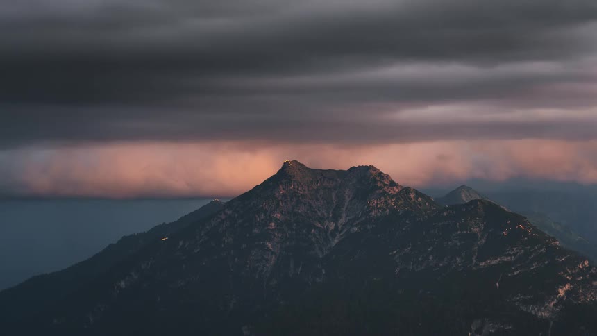Red tinted storm clouds flow over a foggy mountain range