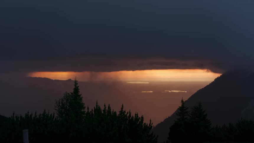 A dark wall cloud kicks off a thunderstorm over mountains and a forest