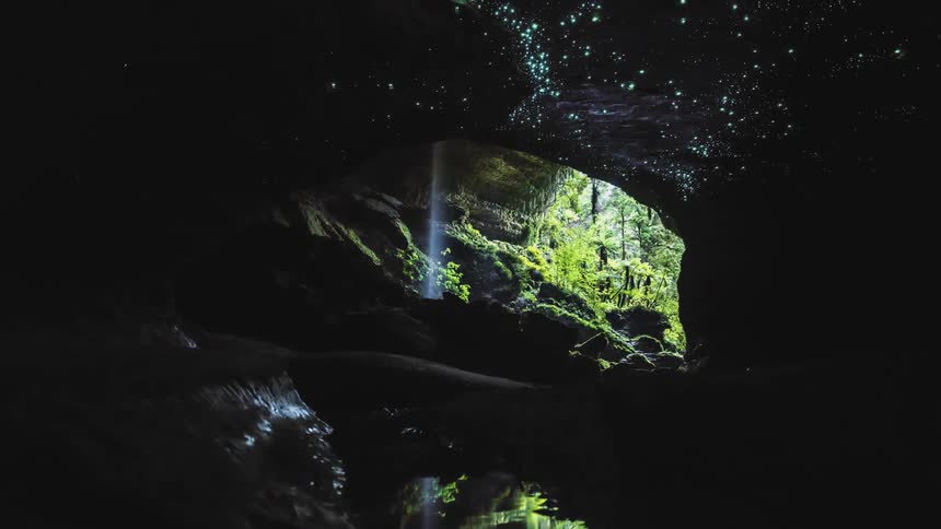 Phosphorescent spots glow on the ceiling of a cavern containing a small waterfall as night falls