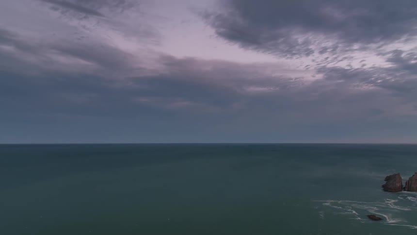 Rocks in the middle of an ocean with the sky getting dark